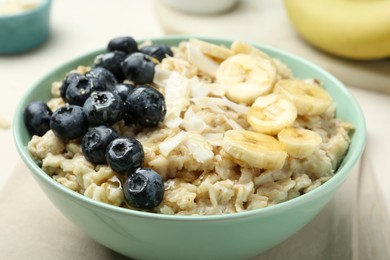 Tasty oatmeal with banana, blueberries, coconut flakes and honey served in bowl on beige table, closeup