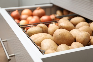 Photo of Open drawer with potatoes and onions, closeup. Orderly storage