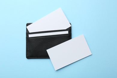 Leather business card holder with blank cards on light blue background, top view