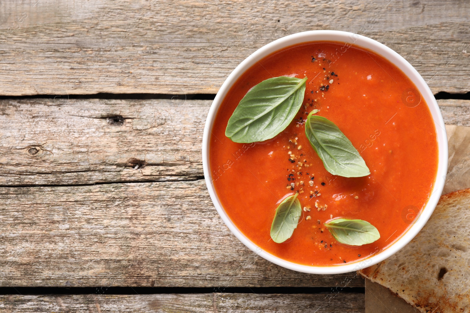 Photo of Delicious tomato soup with basil and spices on wooden table, top view. Space for text