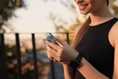 Photo of Happy woman checking pulse with blood pressure monitor on finger after training outdoors, closeup. Space for text