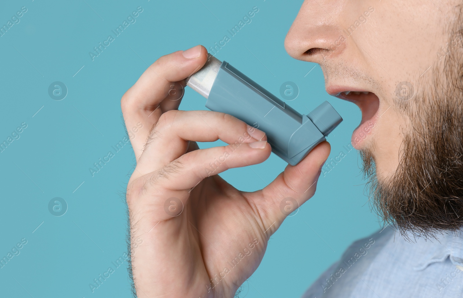 Photo of Young man using asthma inhaler on color background, closeup