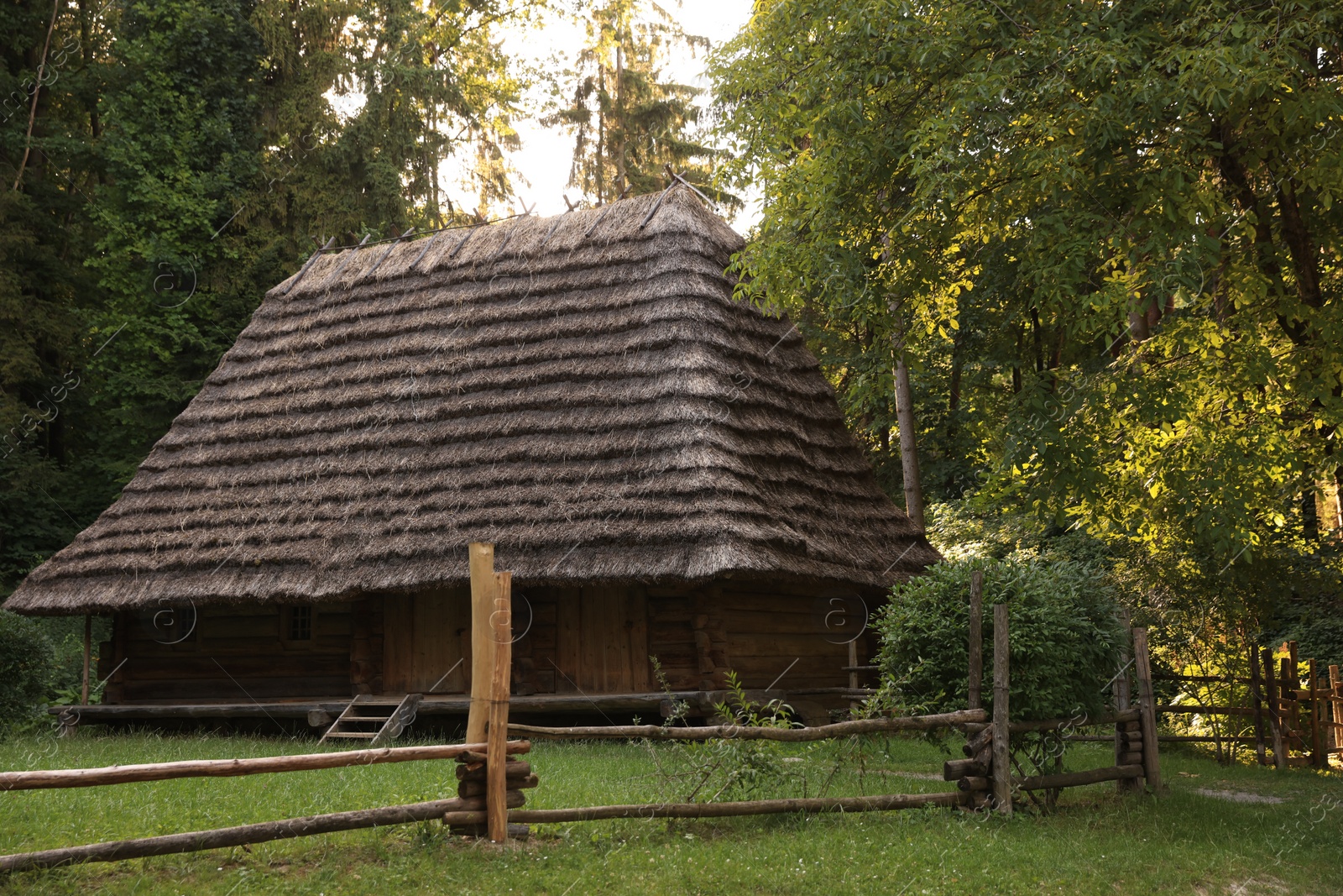 Photo of Old wooden hut with straw roof behind fence in forest