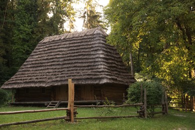 Photo of Old wooden hut with straw roof behind fence in forest