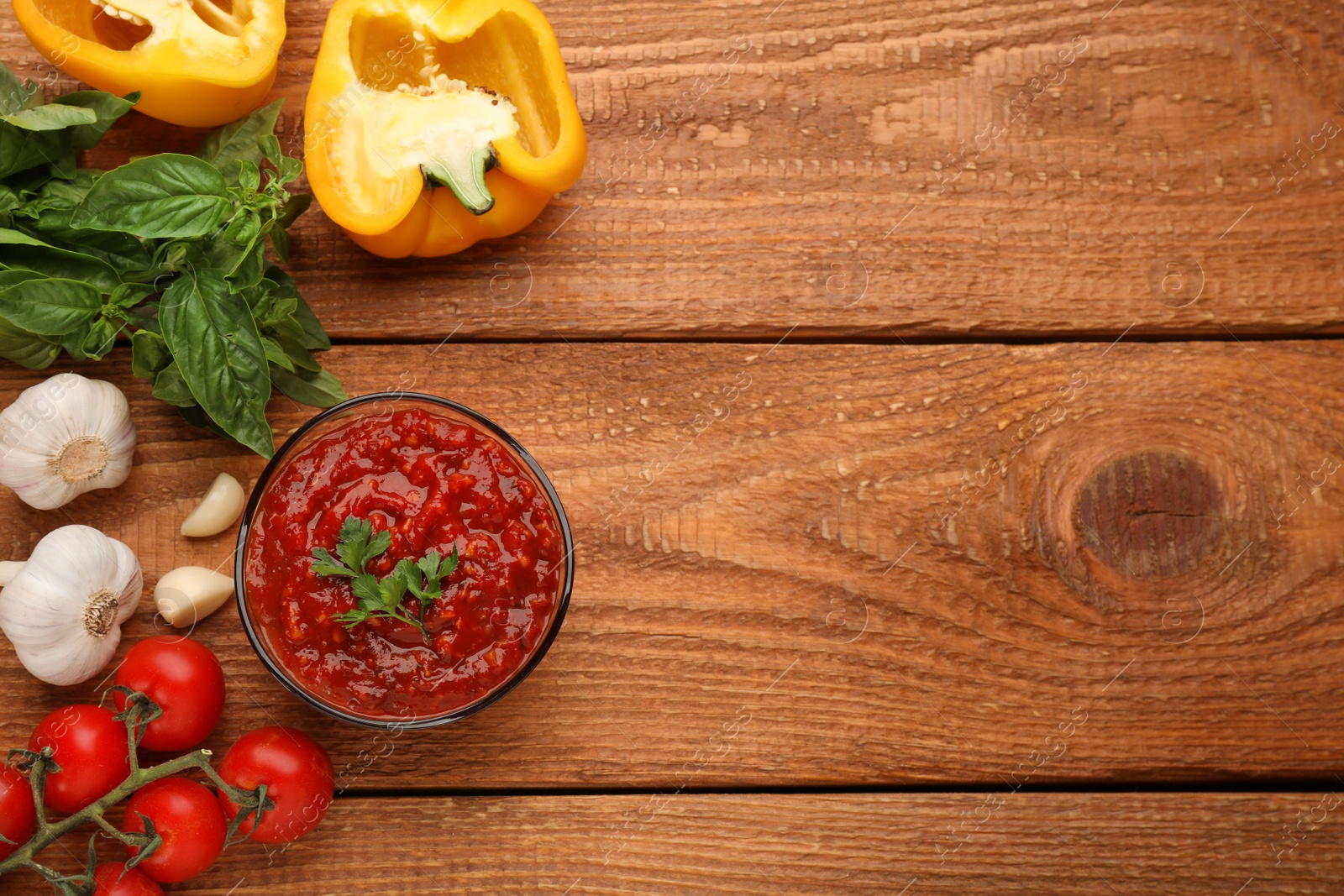 Photo of Delicious adjika sauce in bowl and ingredients on wooden table, flat lay. Space for text