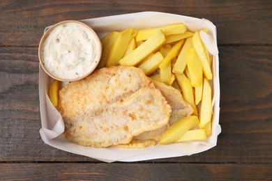 Delicious fish and chips with tasty sauce in paper box on wooden table, top view