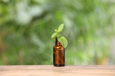 Photo of Bottle with essential oil and mint on wooden table against blurred green background