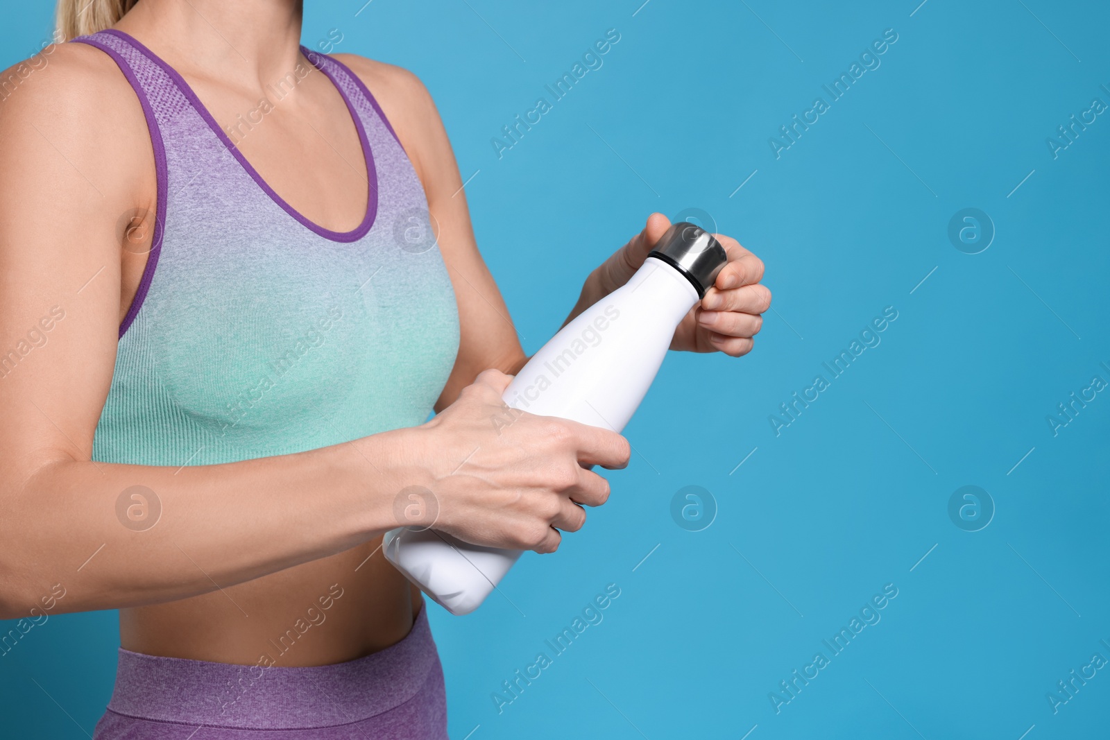 Photo of Sportswoman with thermo bottle on light blue background, closeup. Space for text