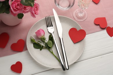Photo of Romantic place setting with flowers and red paper hearts on white wooden table, above view. St. Valentine's day dinner