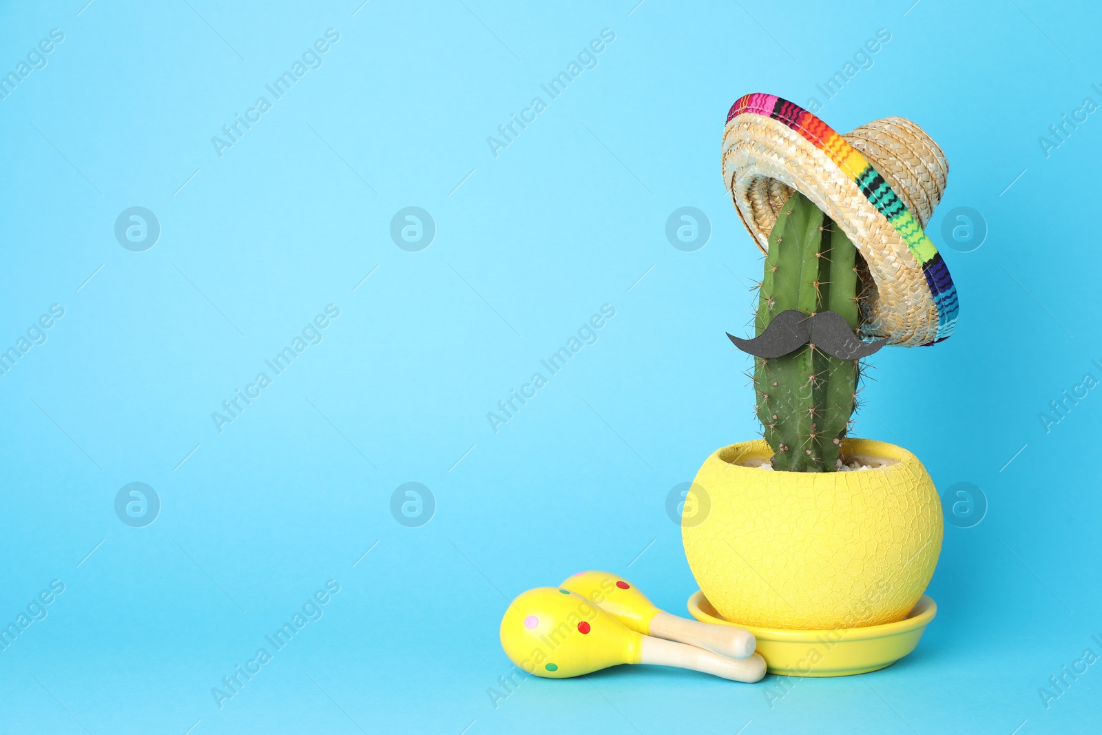 Photo of Mexican sombrero hat, cactus with fake mustache and maracas on light blue background, space for text