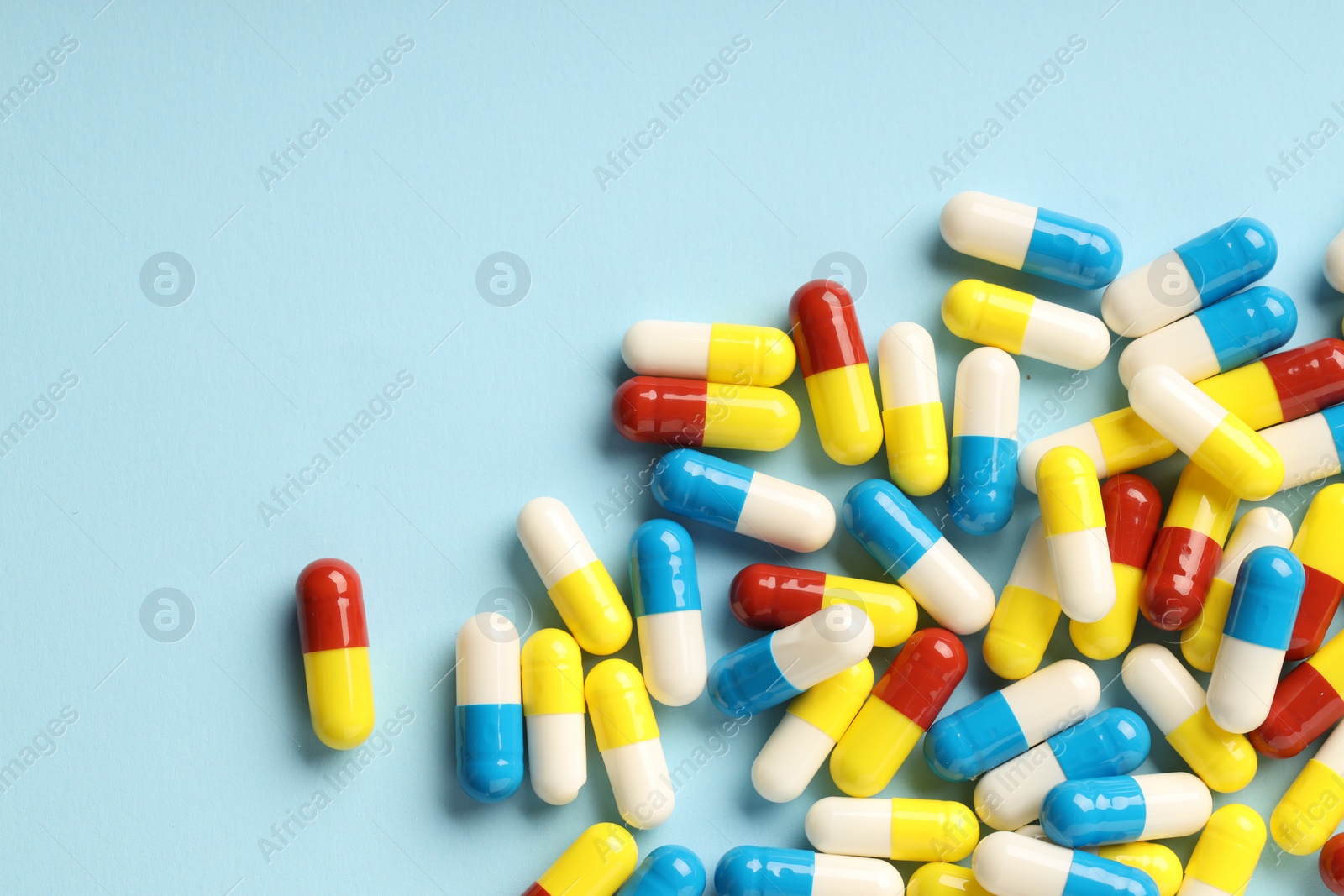 Photo of Many antibiotic pills on light blue background, top view. Space for text