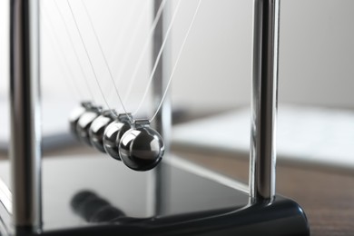 Photo of Newton's cradle on wooden table, closeup. Physics law of energy conservation