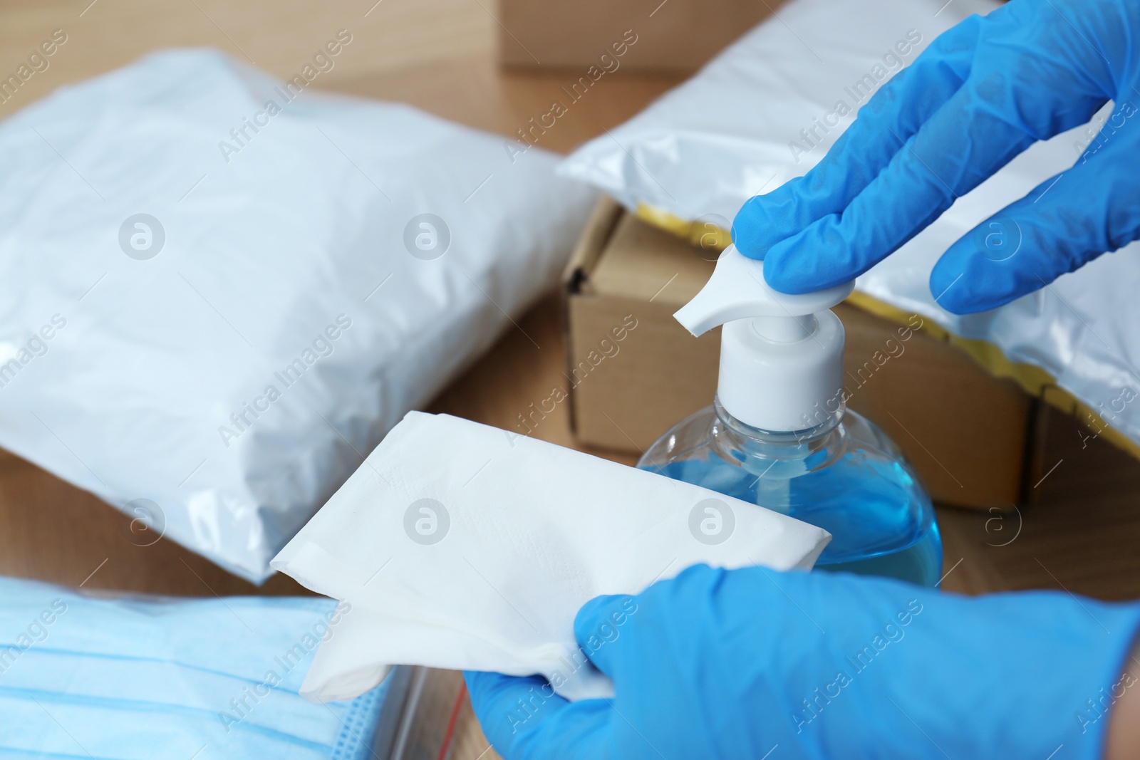 Photo of Woman applying antiseptic gel onto wipe while cleaning parcels at table, closeup. Preventive measure during COVID-19 pandemic