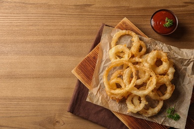 Photo of Flat lay composition with homemade crispy onion rings and tomato sauce on wooden background. Space for text