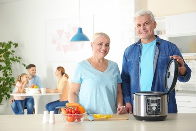 Photo of Mature couple preparing food with modern multi cooker in kitchen
