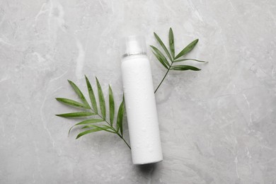 Photo of Dry shampoo spray and green leaves on light grey table, flat lay