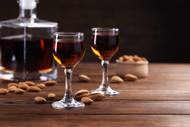 Photo of Liqueur glasses with tasty amaretto and almonds on wooden table, closeup. Space for text