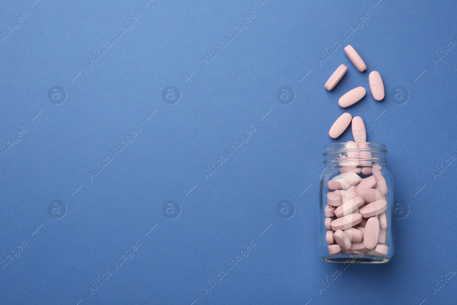 Photo of Bottle of pink vitamin capsules on blue background, top view. Space for text