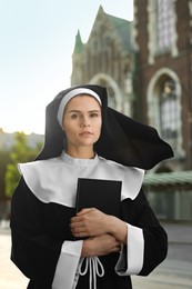 Photo of Young nun with Bible near cathedral outdoors on sunny day