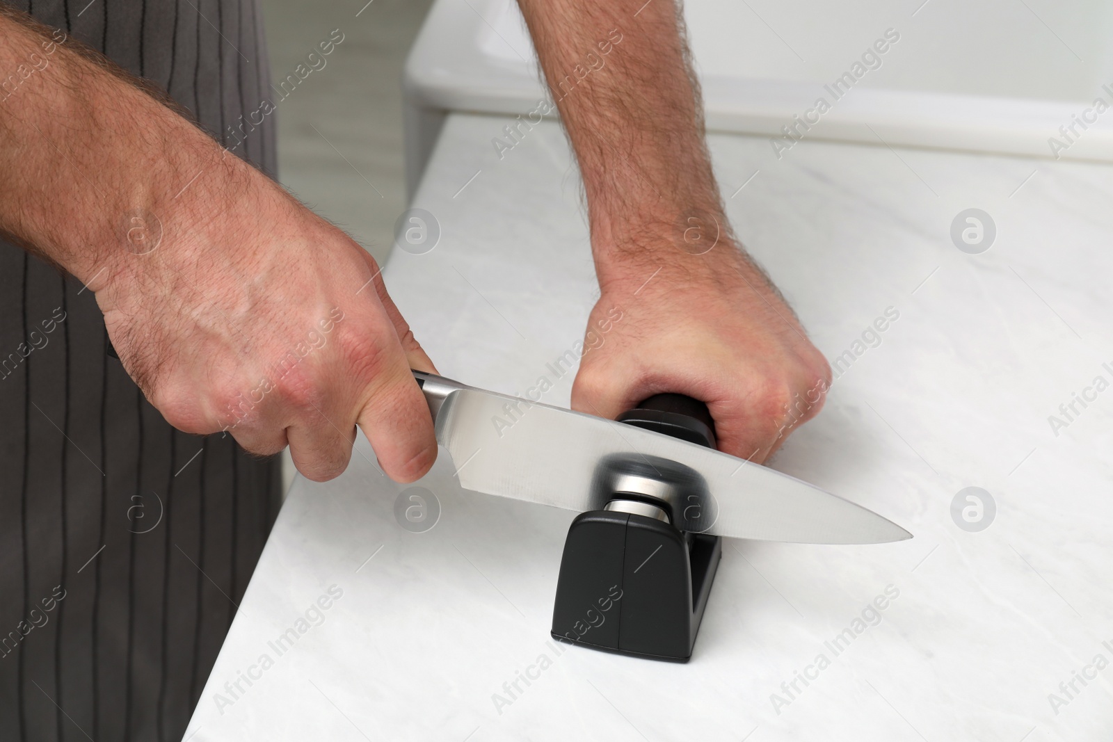 Photo of Man sharpening knife at white table, closeup