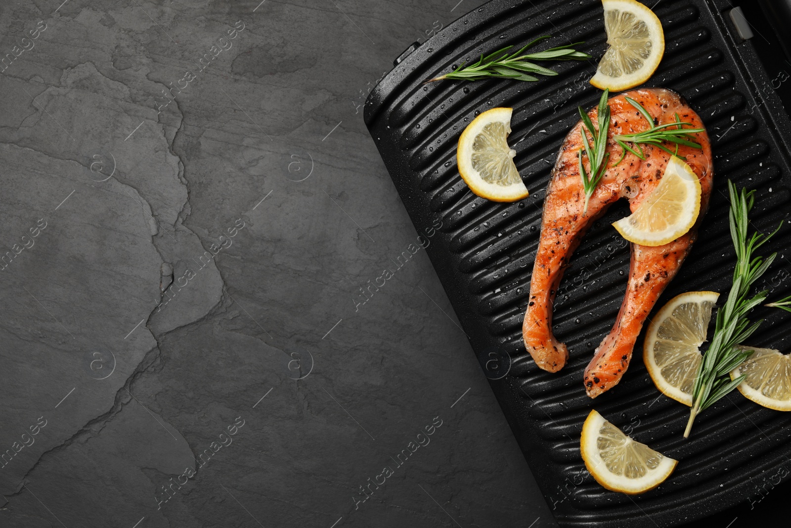 Photo of Cooking salmon. Grill with tasty fish steak, lemon and rosemary on grey table, top view. Space for text