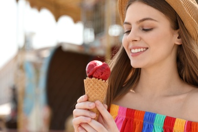 Photo of Young happy woman with ice cream cone in amusement park. Space for text