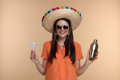 Young woman in Mexican sombrero hat with cocktail and shaker on beige background