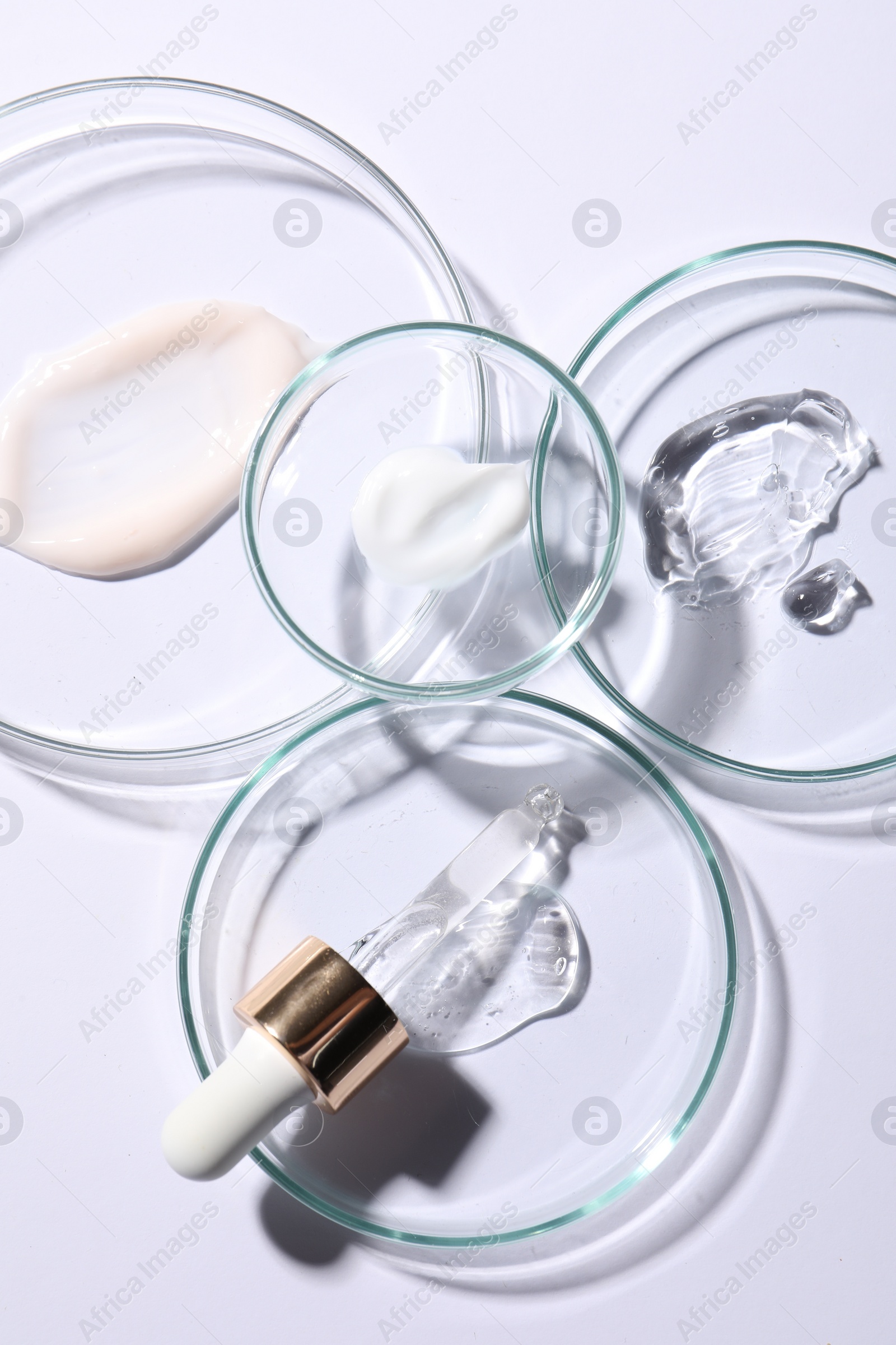 Photo of Petri dishes with samples of cosmetic serums and pipette on white background, flat lay