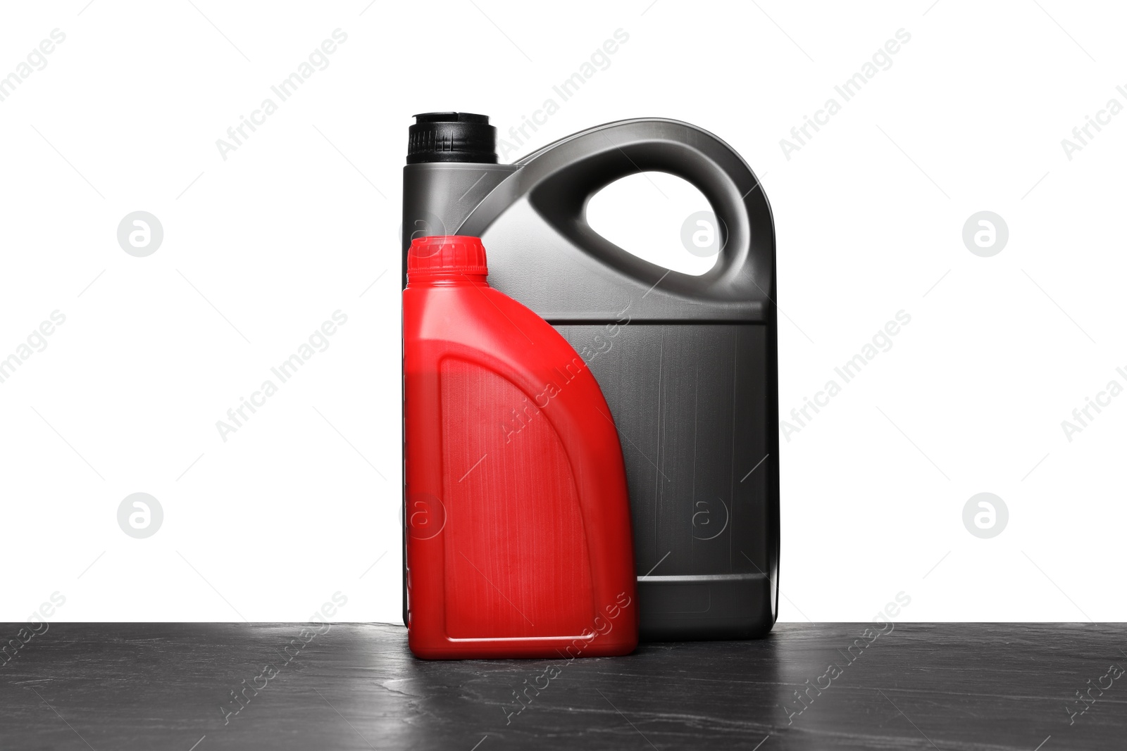 Photo of Motor oil in different canisters on black table against white background