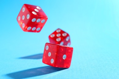 Photo of Three red game dices falling on light blue background, closeup. Space for text