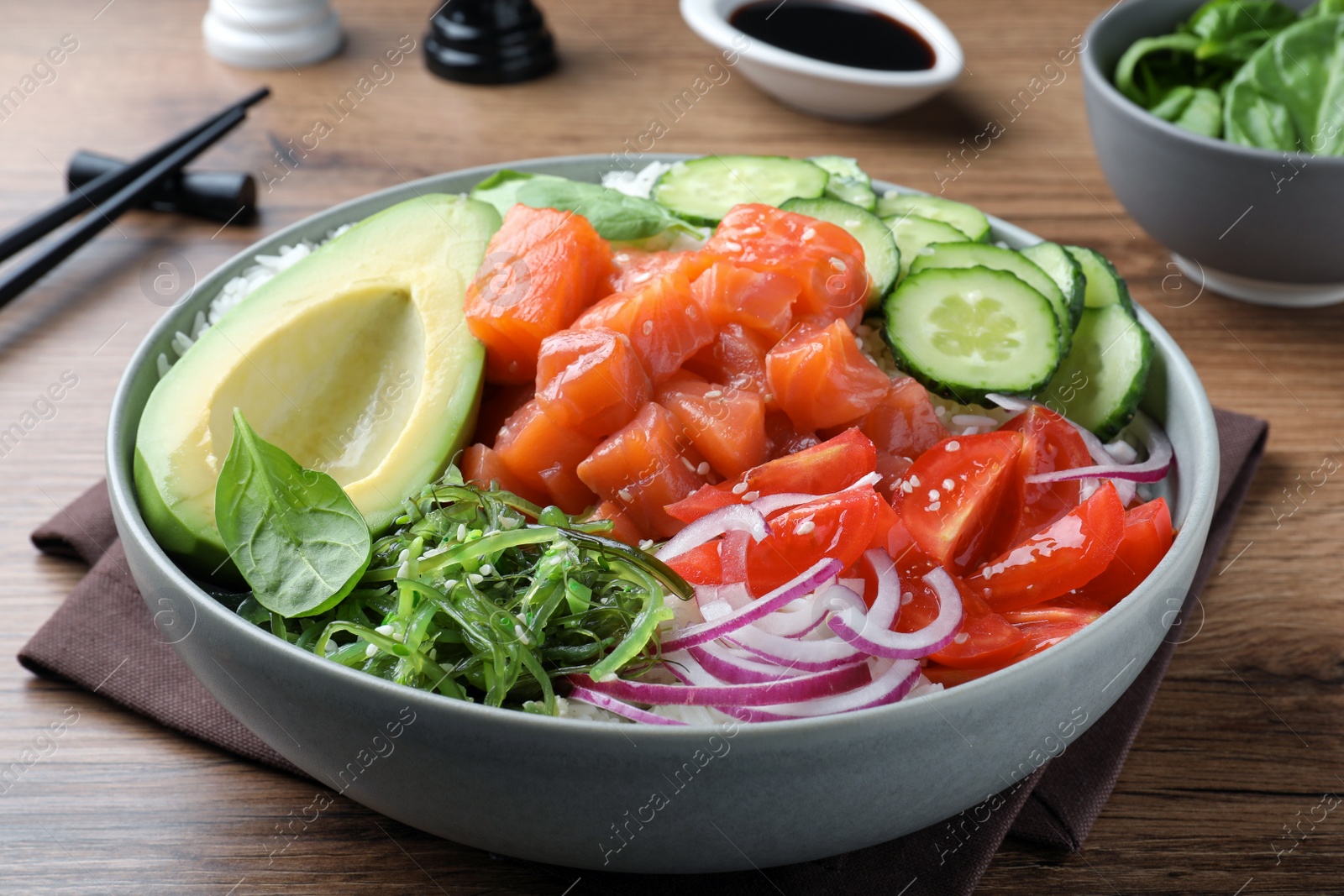 Photo of Delicious poke bowl with salmon and vegetables served on wooden table, closeup