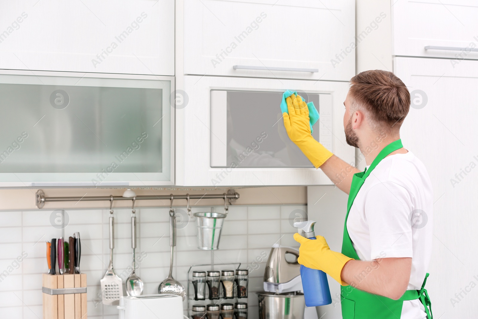 Photo of Young man in uniform cleaning microwave oven in kitchen