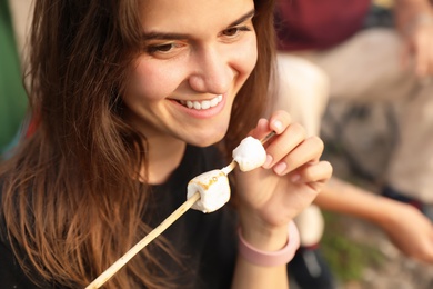 Photo of Young woman with fried marshmallows on skewer outdoors. Camping season