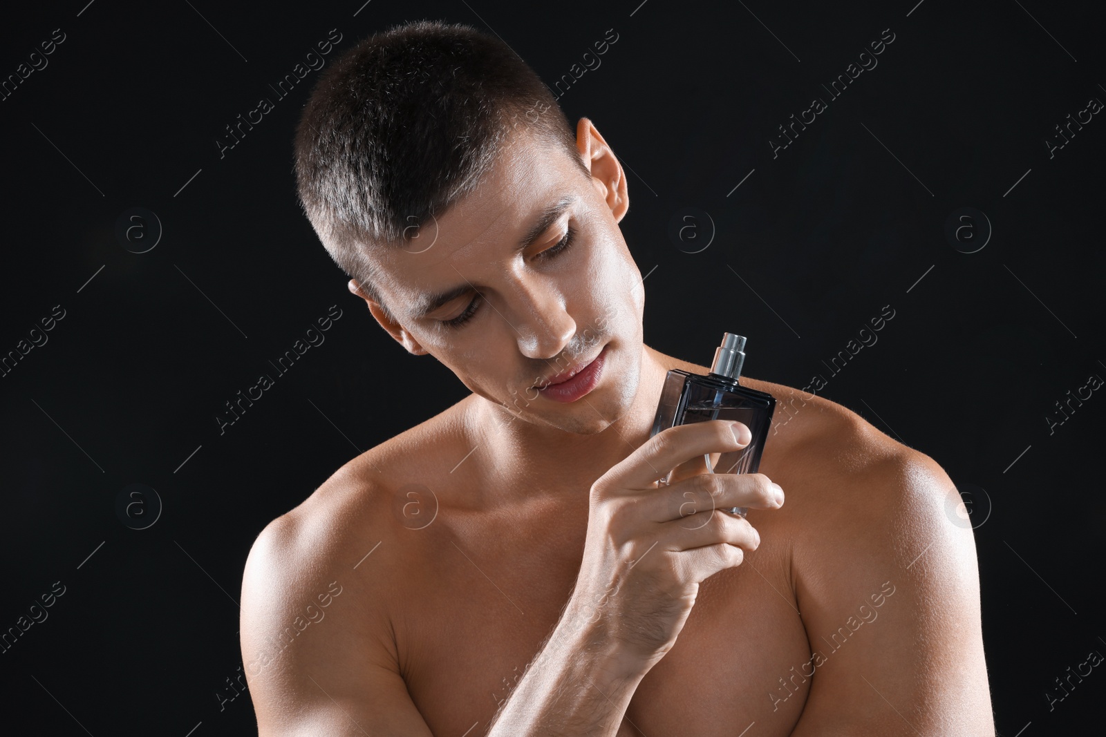 Photo of Handsome young man with bottle of perfume on black background