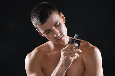 Handsome young man with bottle of perfume on black background