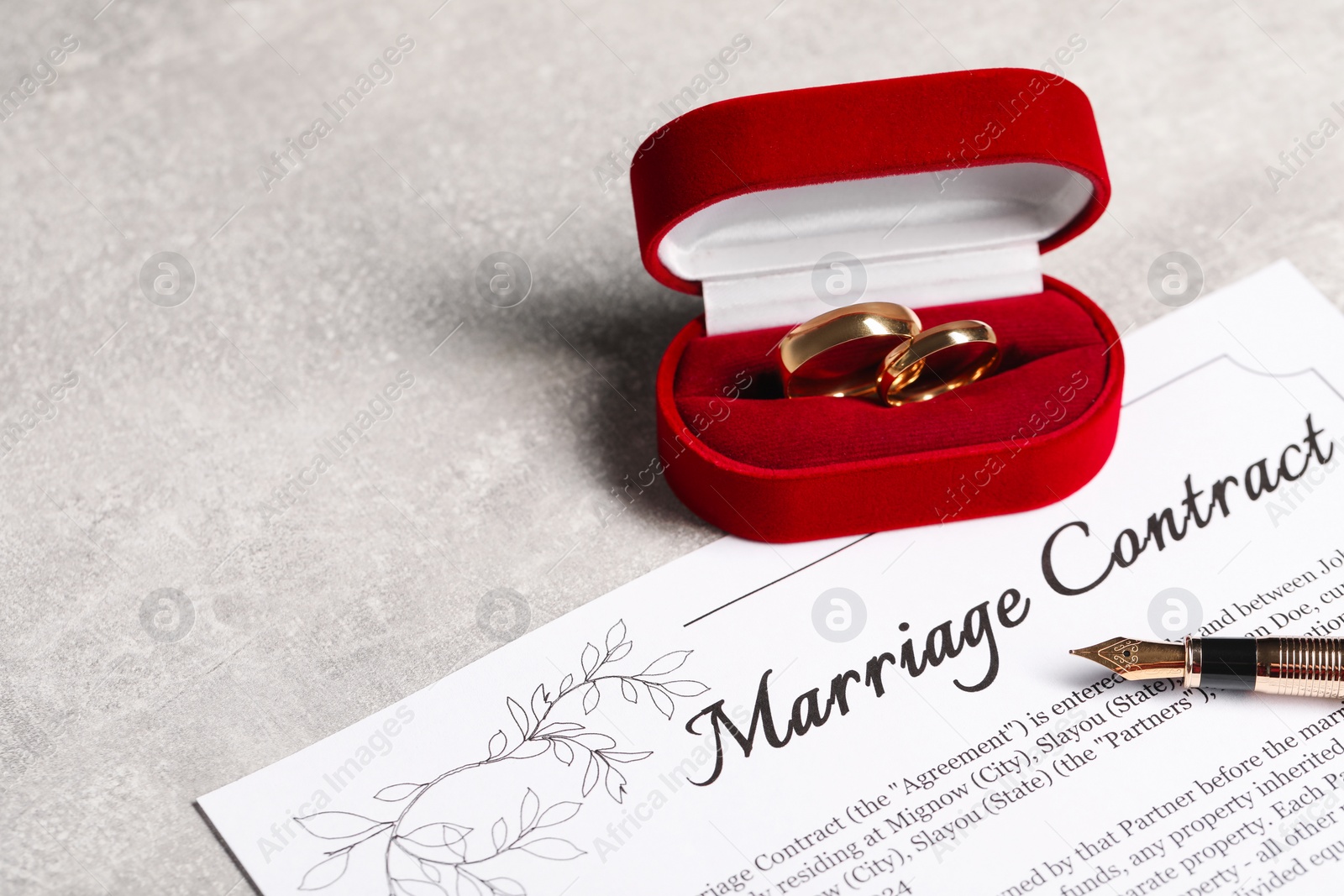 Photo of Marriage contract, fountain pen and golden wedding rings on grey table