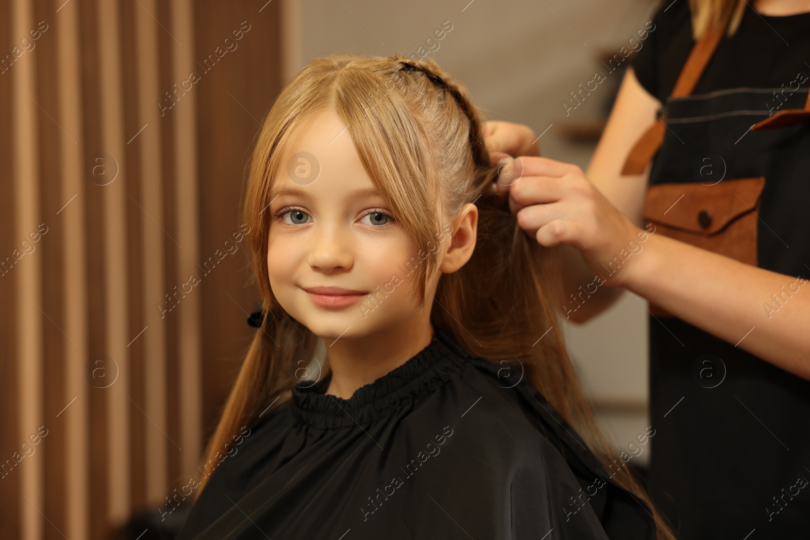 Photo of Professional hairdresser braiding girl's hair in beauty salon, closeup