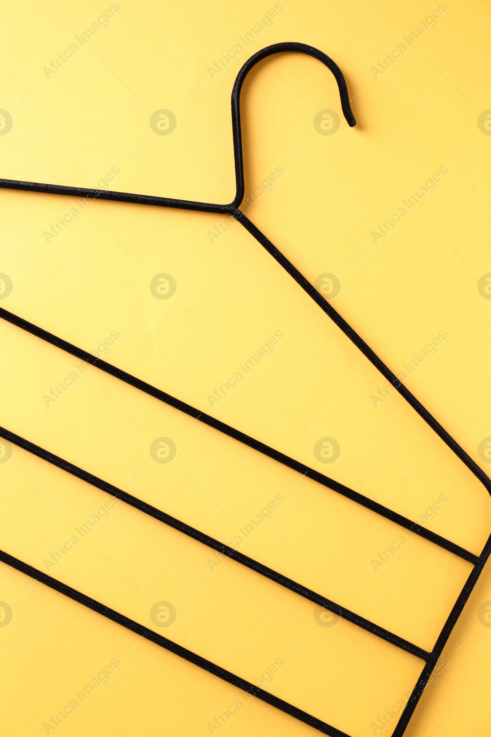 Photo of One black hanger on yellow background, top view