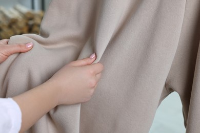 Photo of Woman touching clothes made of soft beige fabric indoors, closeup