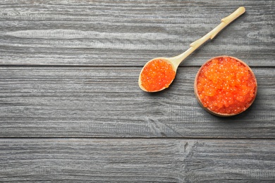 Photo of Bowl and spoon with delicious red caviar on wooden background