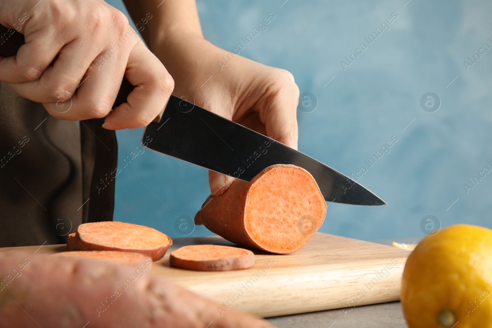 Photo of Woman cutting sweet potato on wooden board, closeup