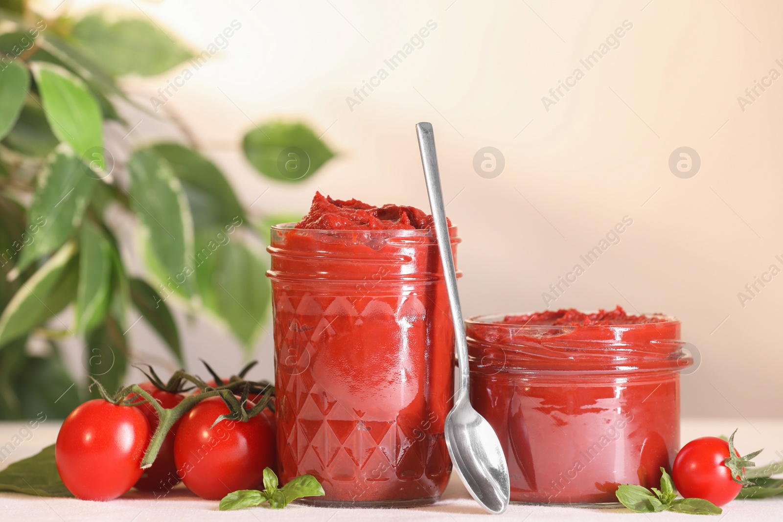 Photo of Jars of tasty tomato paste, spoon and ingredients on white table