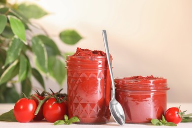 Photo of Jars of tasty tomato paste, spoon and ingredients on white table