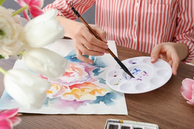 Woman painting flowers with watercolor at wooden table, closeup. Creative artwork