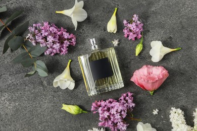 Bottle of luxury perfume and floral decor on dark grey table, flat lay