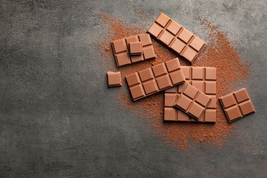 Photo of Delicious milk chocolate and cocoa powder on grey table, flat lay. Space for text