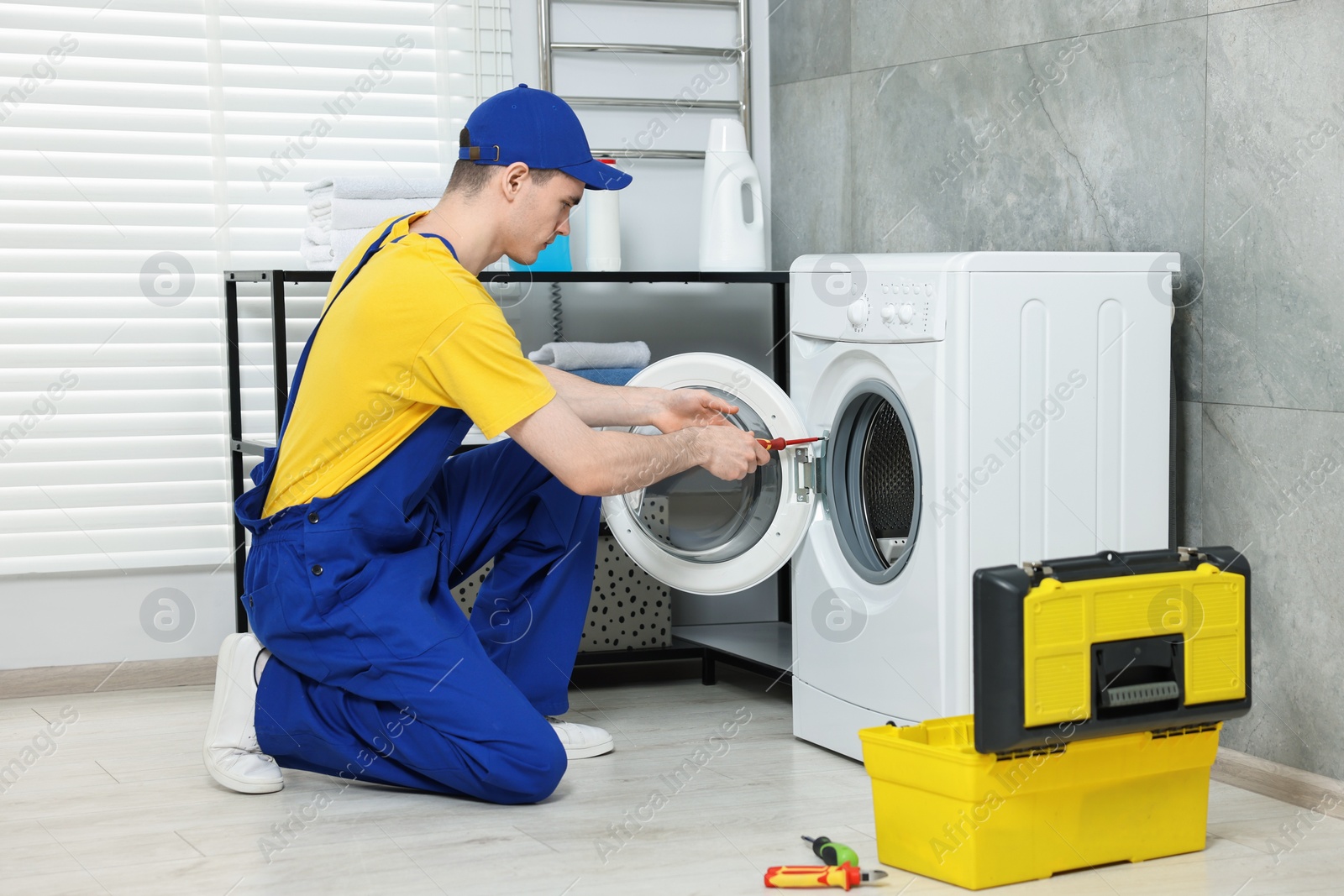 Photo of Young plumber repairing washing machine in bathroom