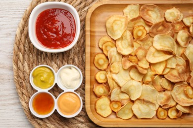 Tasty homemade parsnip chips with different sauces on white wooden table, flat lay