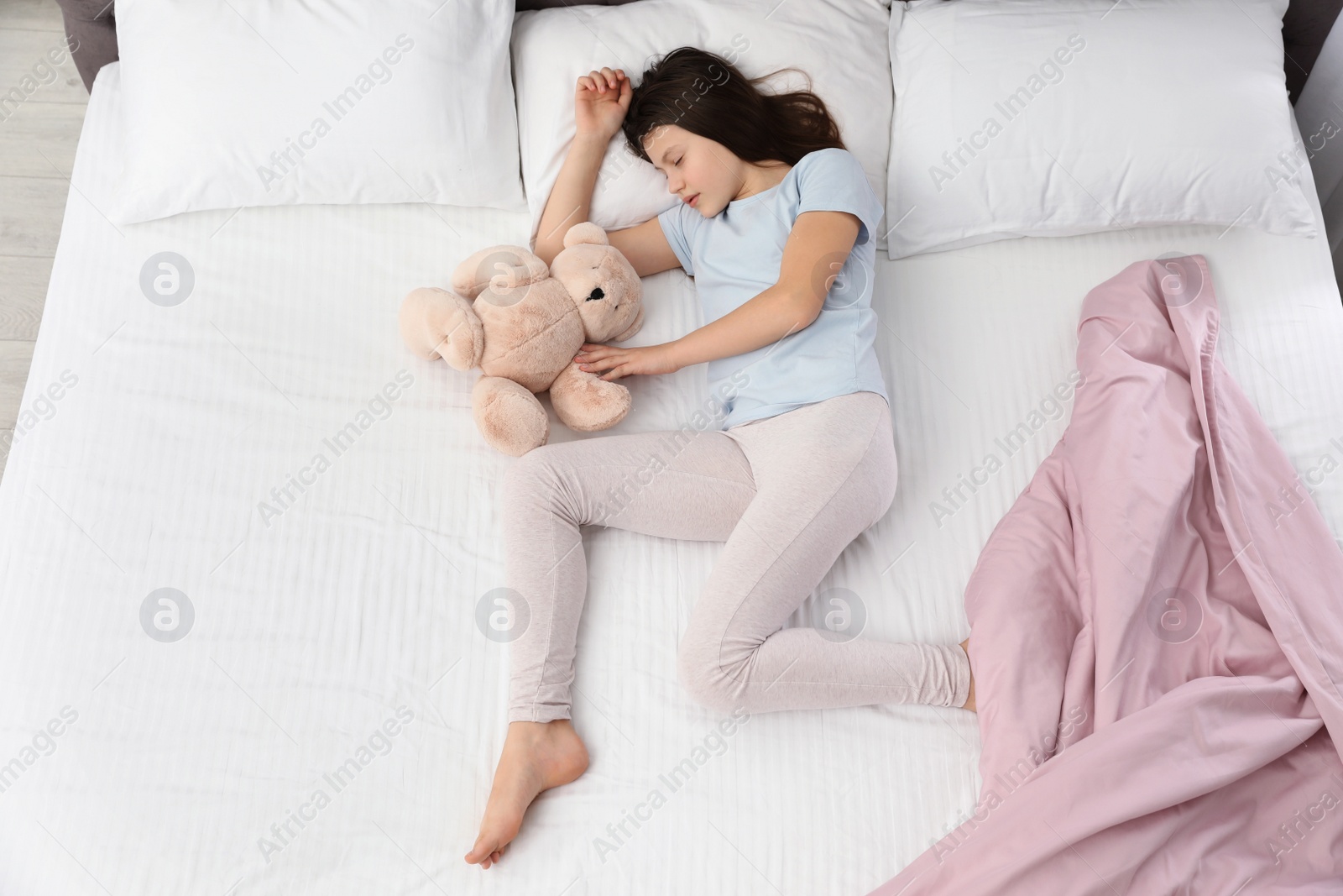 Photo of Beautiful little girl with teddy bear sleeping in bed, top view