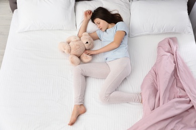 Beautiful little girl with teddy bear sleeping in bed, top view